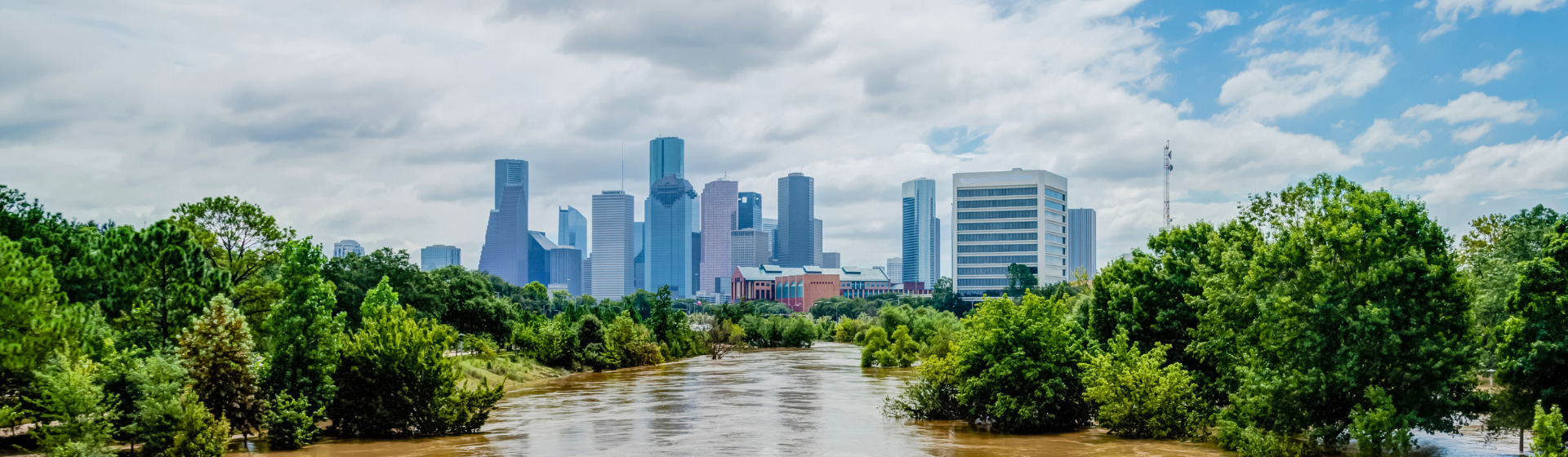 High and fast water rising in Bayou River with downtown Houston in background under cloud blue sky.