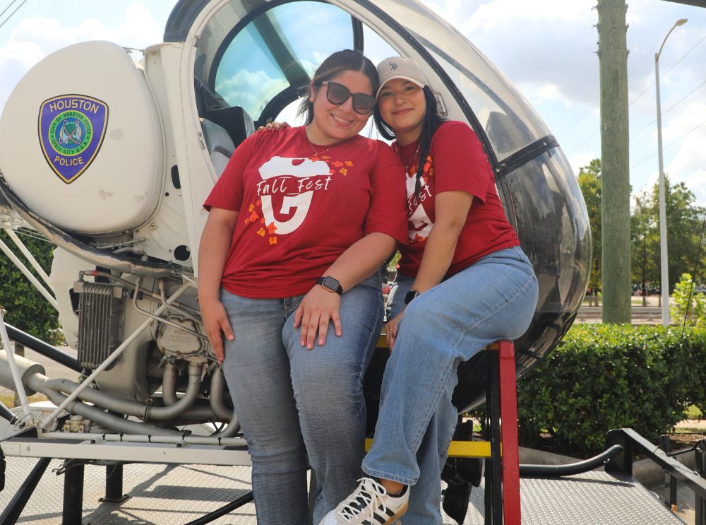 Image of two women Hispanic employees at a fall fest posing with a Houston Police Department helicopter