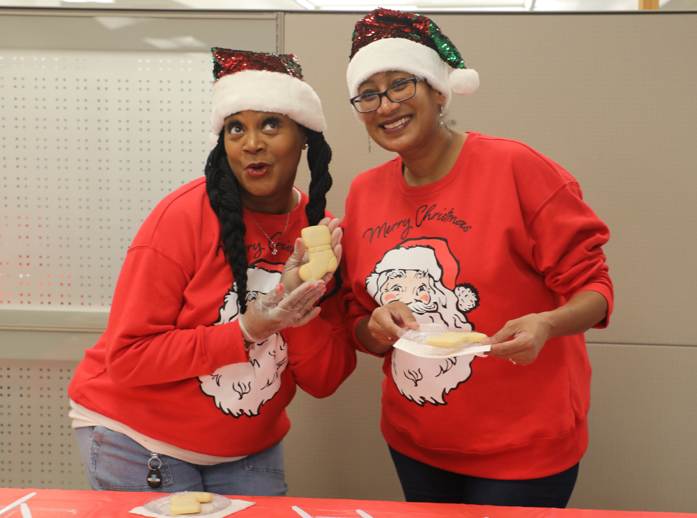 Two HPCU employees volunteering at a Christmas event at a cookie station smiling and posing