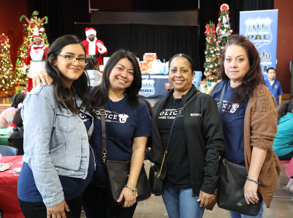 Four Houston Police Credit Union employees smiling for a picture at a volunteer Christmas event to help youth