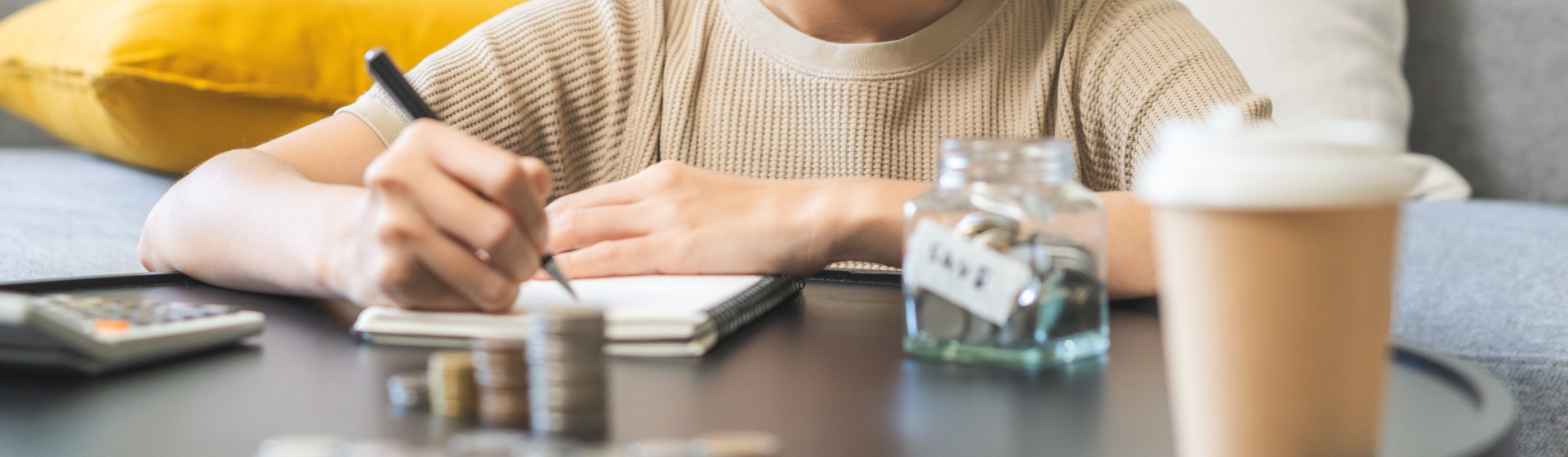 Woman writing down budget with money jar in front of her