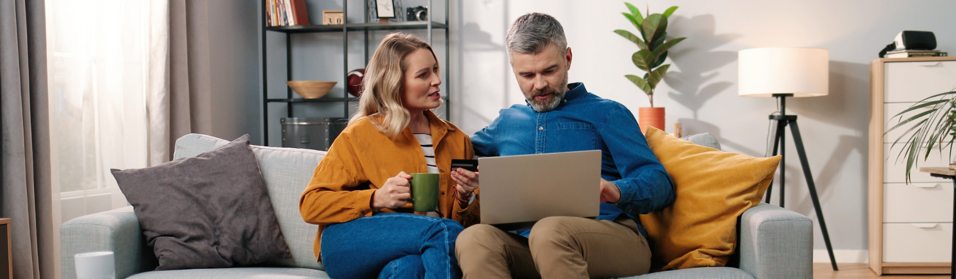 Caucasian middle-aged married couple sitting on sofa at home making payment with credit card on laptop computer