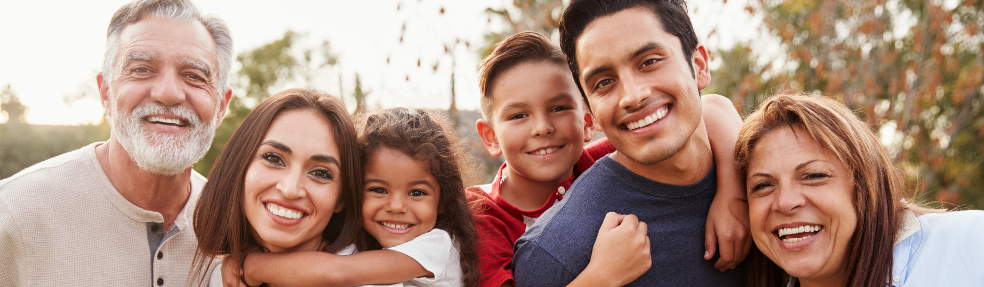 Three generation Hispanic family standing in the park, smiling to camera.